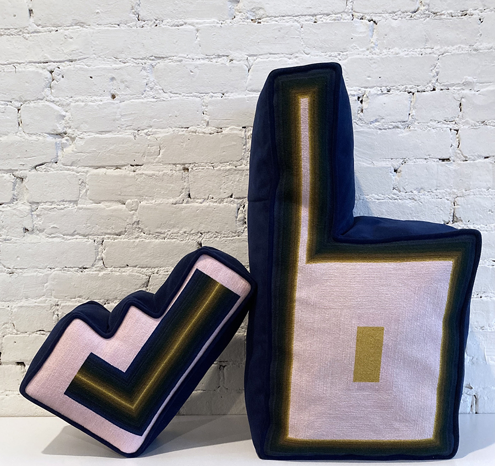 Two shaped needlepoint pillows leaning against each other
