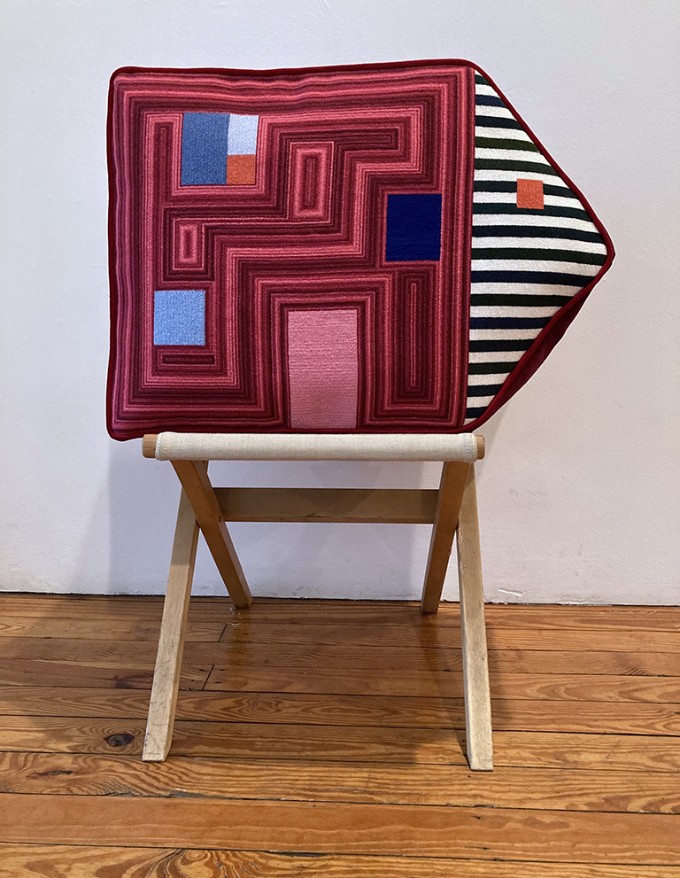 Shaped needlepoint pillow on a folding stool