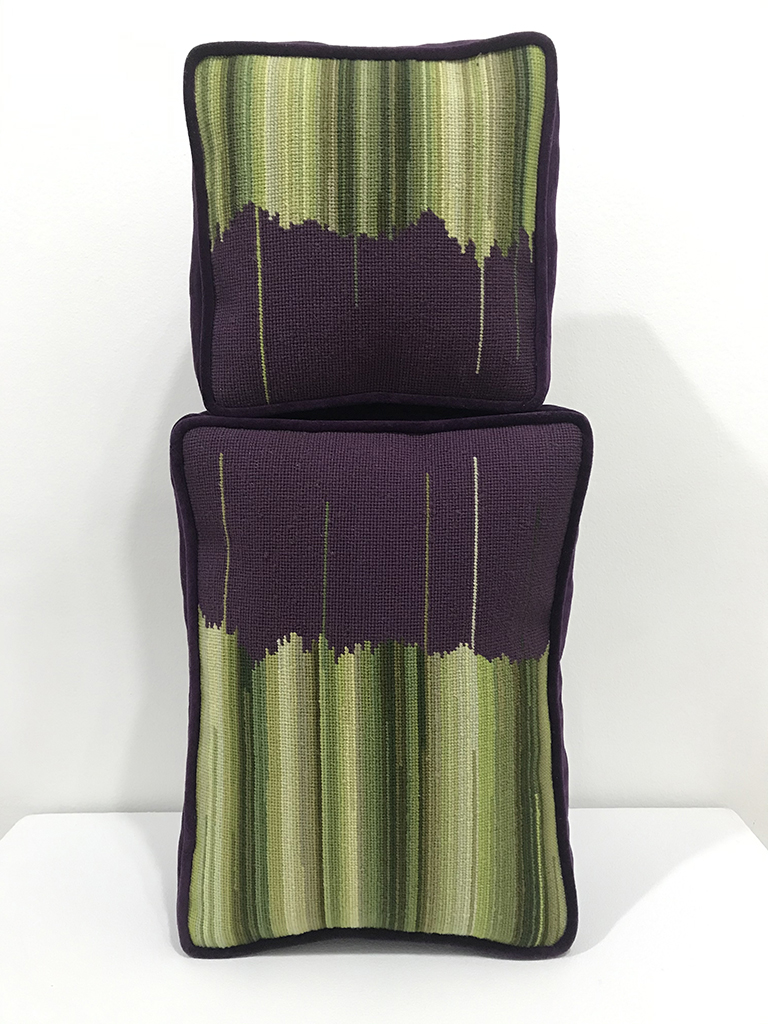One green and brown needlepoint pillow on top of another green and brown needlepoint pillow
