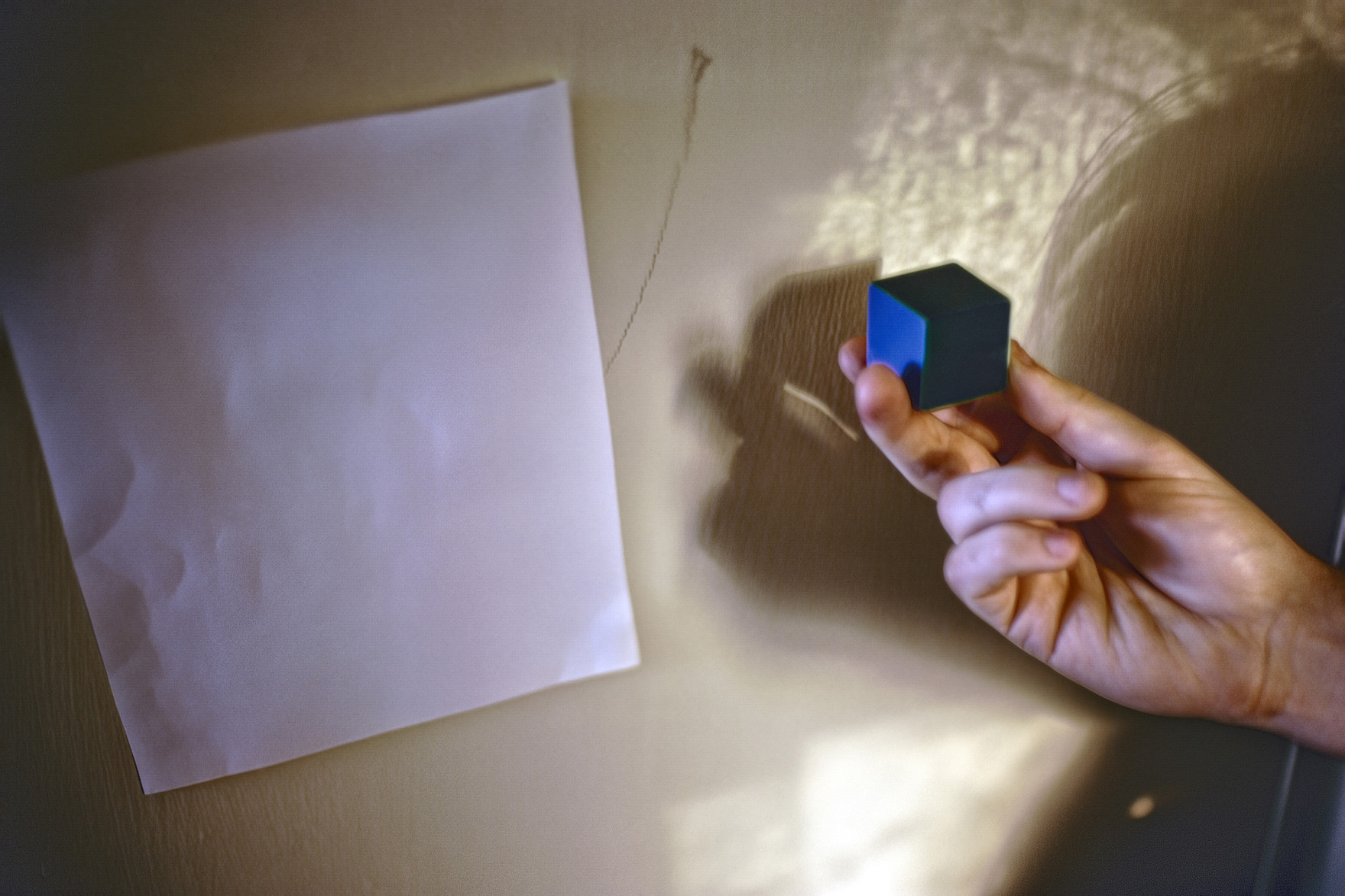 hand holding a blue cube in front of a sheet of paper